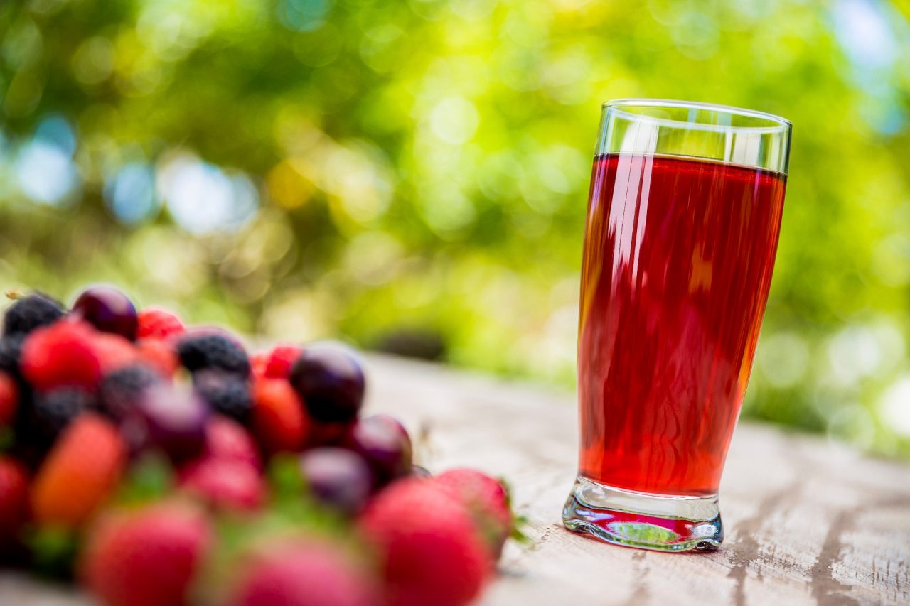 A glass of berries juice and berries on outdoor table